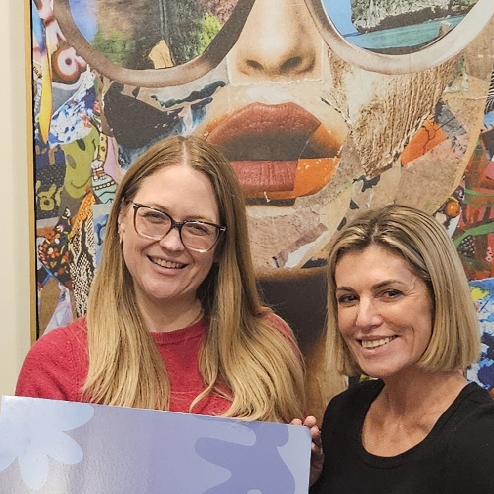 Jess Morris and Jen McClain of Vital Balance 10 smiling in front of a colorful collage mural